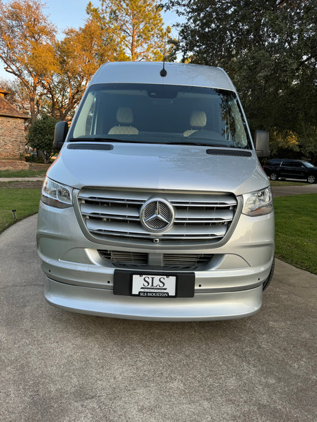 Silver Mercedes-Benz Sprinter van, ideal for rv rental, on a residential driveway. Features a large grill and emblem.