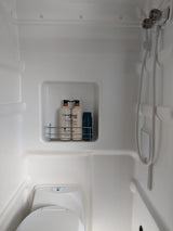 A functional white wet bath in an rv rental, equipped with a toilet, handheld shower, and a caddy holding shampoo and conditioner.