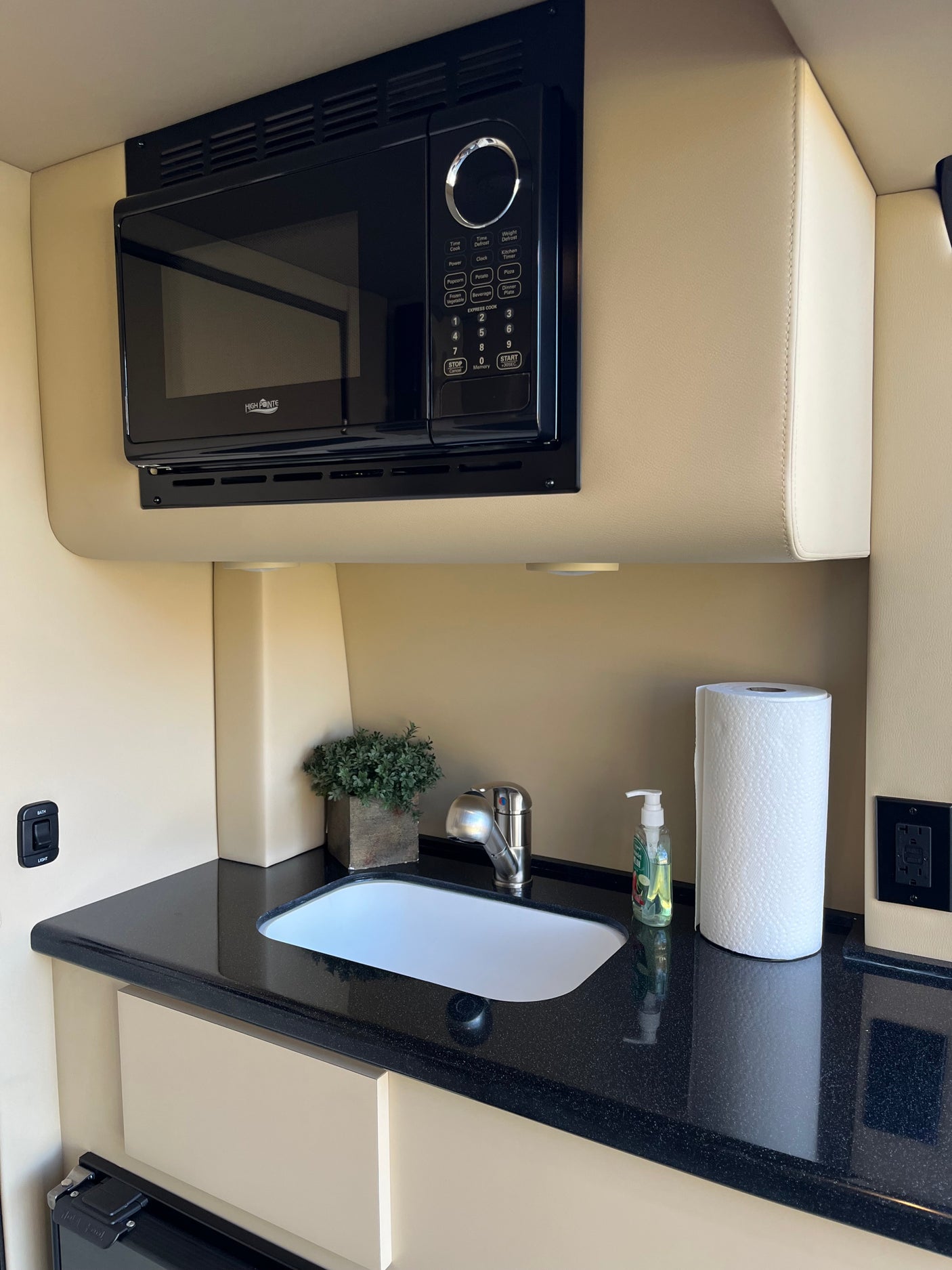 RV rental: Compact kitchen featuring an overhead microwave, sink, black countertop, soap, and paper towels.