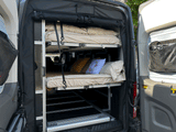 View inside an RV rental showing stacked bunk beds, a bottom storage tray, and the organized cargo area of a camper van.