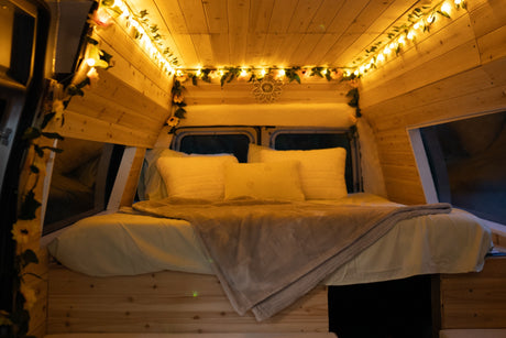 Cozy RV rental bedroom featuring wood walls, string lights with greenery, a sunflower accent, and a plush bed.