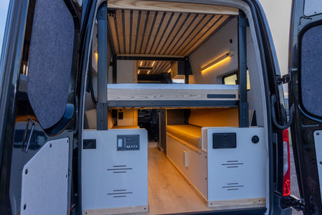 Inside an RV rental, a custom camper van features adjustable bunk beds, wood accents, and integrated controls, viewed from the rear.