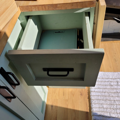 Organized storage in an RV rental: An open sage-green drawer reveals a teal cutting board, with wooden floors and a rug.