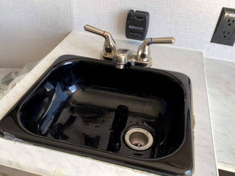 RV rental interior: A black sink with chrome faucet, white countertop, and wall-mounted controls.
