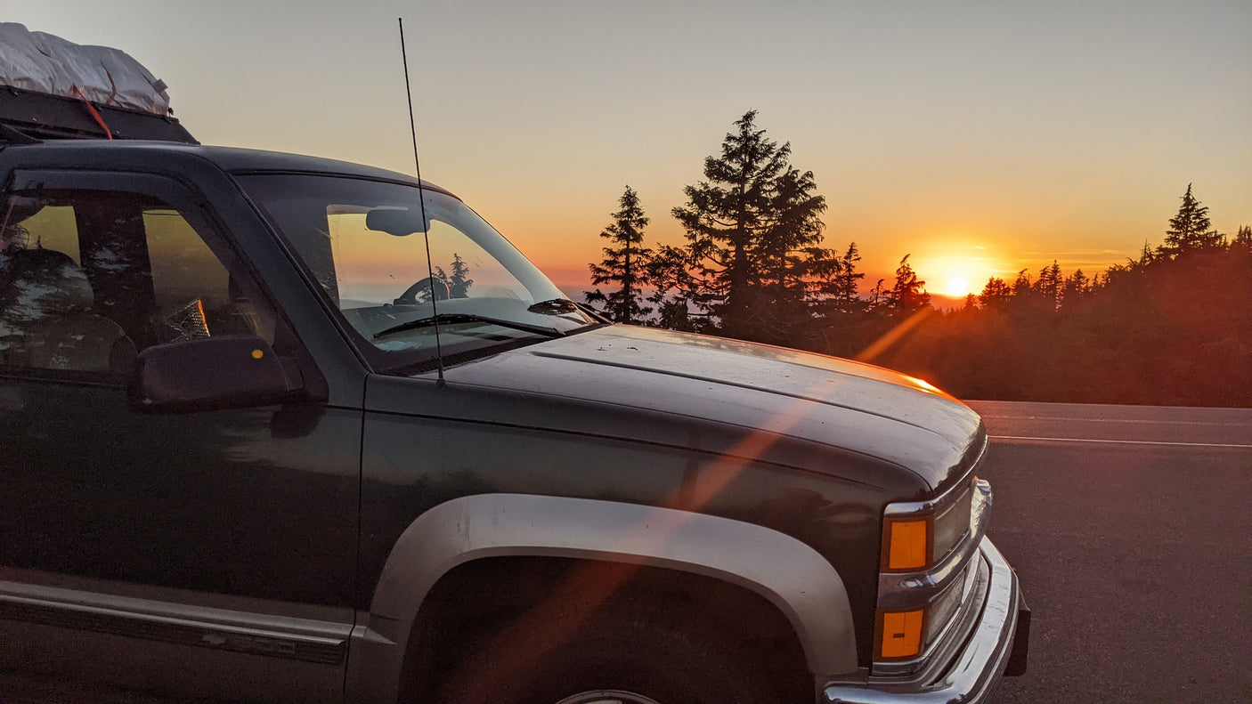 An RV rental vehicle parked at sunset, with evergreen trees silhouetted against the vibrant orange sky. Perfect for an outdoor road trip.