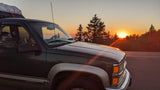 An RV rental vehicle parked at sunset, with evergreen trees silhouetted against the vibrant orange sky. Perfect for an outdoor road trip.