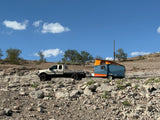 RV rental adventure! A sturdy truck tows a blue & orange pop-up camper on a rugged, rocky desert trail under blue skies.