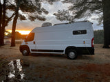 White RV rental van parked by a lake at stunning sunset. Ideal for a nature camping adventure, complete with power hookup.