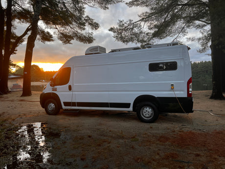 White RV rental van parked by a lake at stunning sunset. Ideal for a nature camping adventure, complete with power hookup.
