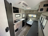 RV rental interior: a compact kitchenette with stove/sink, dinette area, and wood flooring.