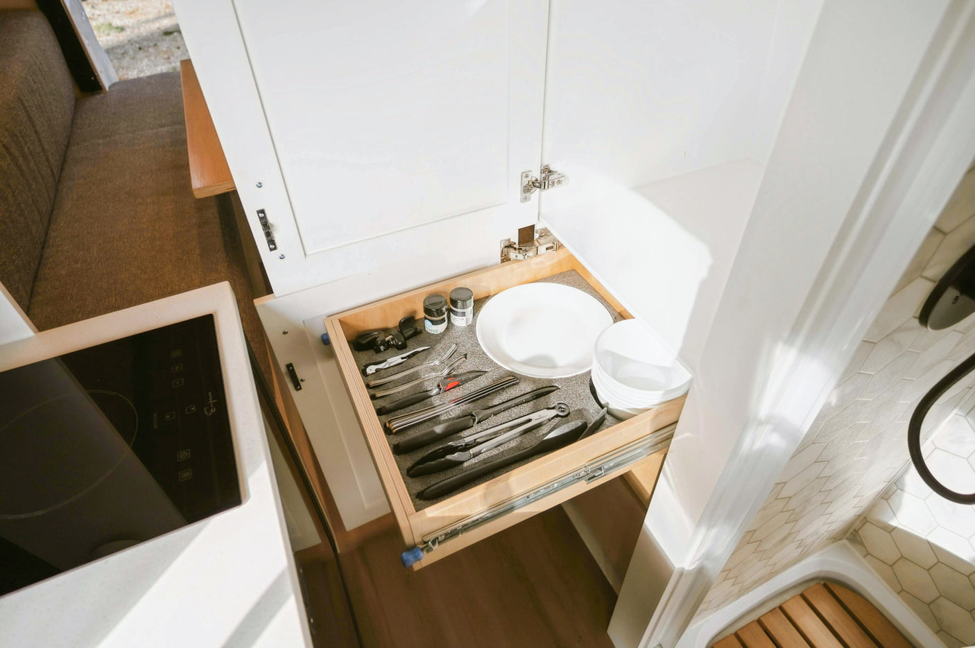 Compact RV rental kitchen: a pulled-out drawer with organized utensils, plates, and bowls, next to a cooktop.