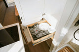 Compact RV rental kitchen: a pulled-out drawer with organized utensils, plates, and bowls, next to a cooktop.