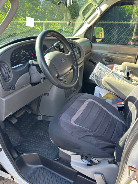 Interior of an RV rental van: Driver's view with Ford steering wheel, dashboard, seat cover, and sunshade. Ready for adventure.