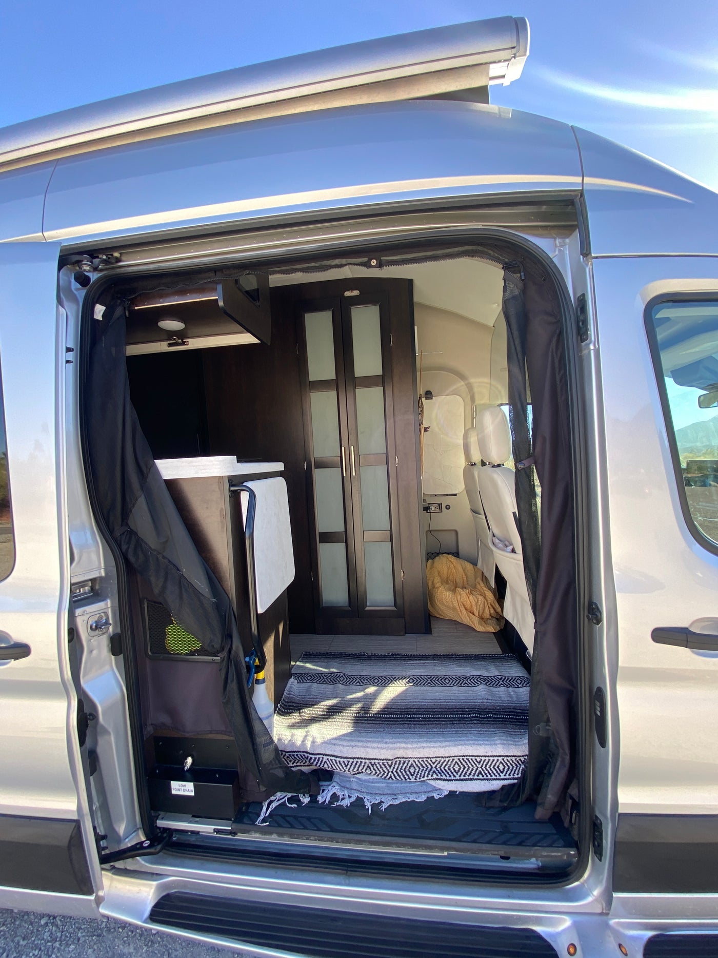 Inside an rv rental camper van: open door reveals a cozy interior with cabinetry, seats, and a patterned rug. — photo 12