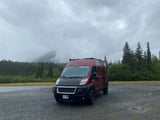 Red RV rental camper van parked on gravel in misty Alaska mountains. Perfect for your next adventure!