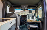 RV rental interior shows a compact kitchenette, swiveling passenger seat with a portable table, and a scenic view.