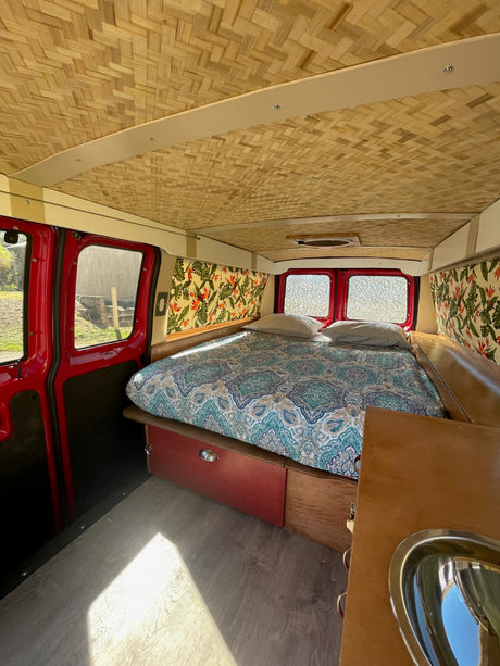 Tropical RV rental interior with bamboo ceiling, comfy bed, and kitchenette. Perfect camper van conversion.