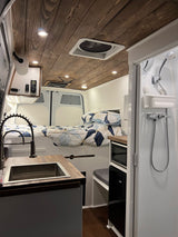 Cozy RV rental interior: bed, kitchen, & shower in a modern camper van with a beautiful wooden ceiling.