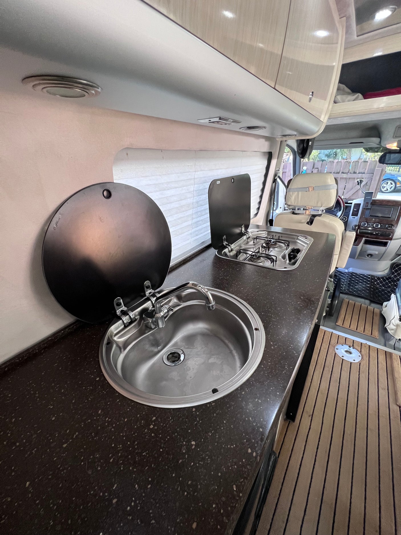 RV rental kitchenette with stainless steel sink, two-burner stove, dark counter, and light wood overhead cabinets.