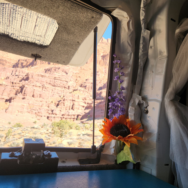 Scenic desert views from inside an RV rental. A window opens to red rock formations; flowers adorn the cozy interior. — photo 10