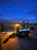 Evening RV rental setup with bikes, dog, and awning under a blue sky, perfect for desert camping and adventure.