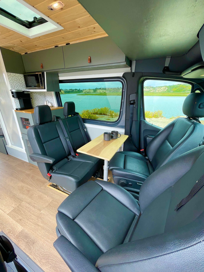 Inside this modern RV rental: comfy seating, a wooden table with mugs, compact kitchen, & panoramic river views. Ideal for camper van adventures. — photo 4