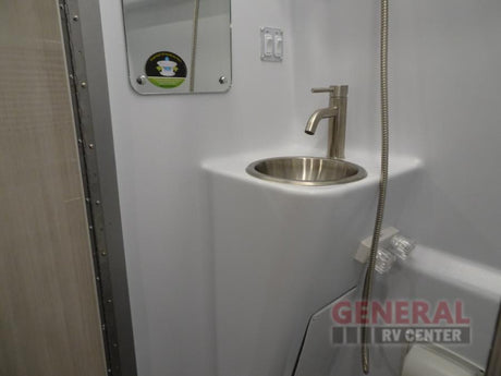 This RV rental's compact bathroom features a stainless steel sink, modern faucet, mirror, and shower, perfect for travel.