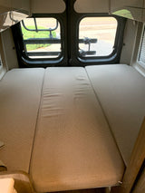 Cozy RV rental camper van interior. A three-panel bed is visible, with rear windows showing a road and bike rack.