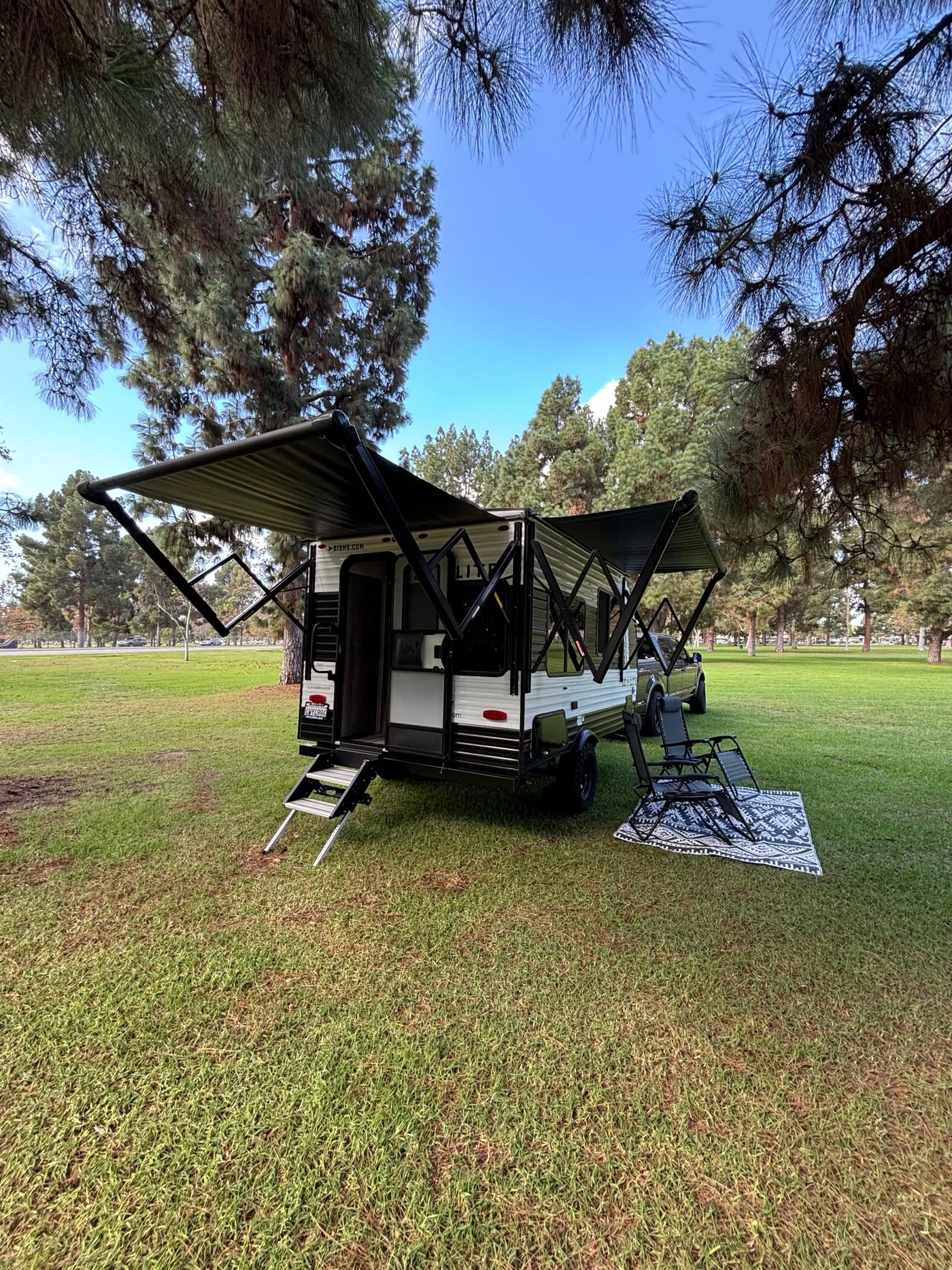 RV rental set up for comfort: a travel trailer with extended awnings, steps, chairs, and a rug on green grass. — photo 4