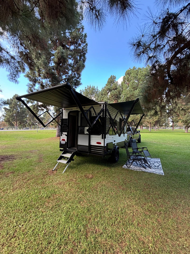 RV rental set up for comfort: a travel trailer with extended awnings, steps, chairs, and a rug on green grass. — photo 4