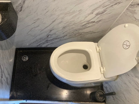 RV rental toilet with lid up, showing "no standing" symbol. Compact design on black base with drain and brush.