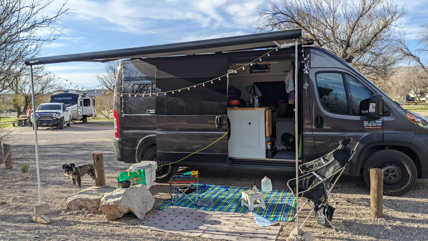 Spacious camper van RV rental set up at a sunny campsite with a dog, awning, and outdoor gear for comfortable travel.