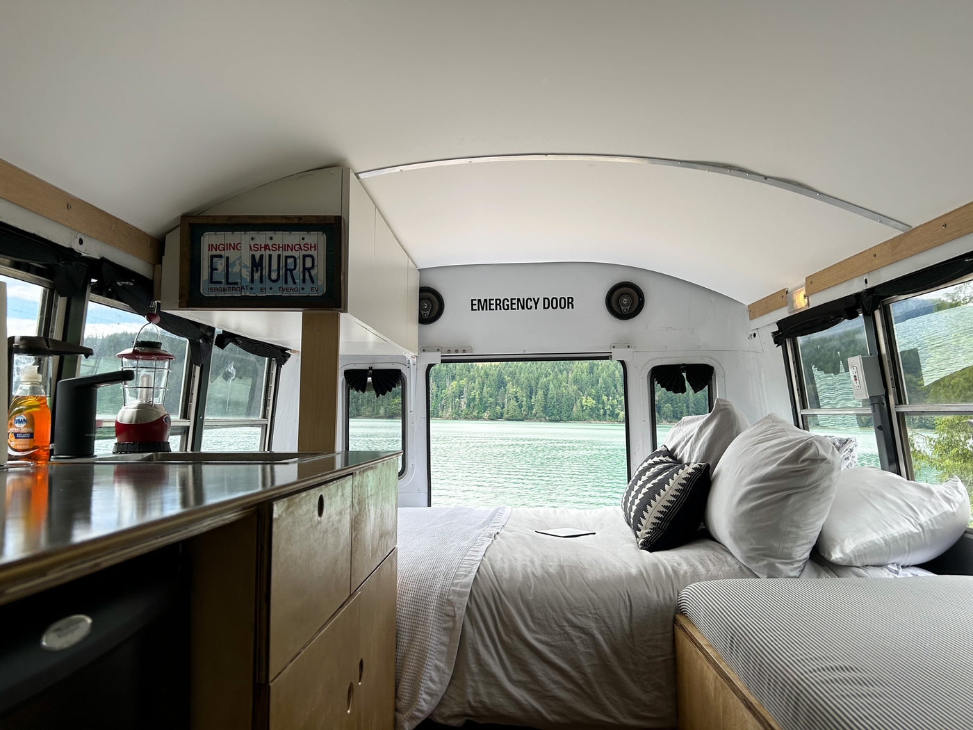 Scenic RV rental bus conversion featuring a comfy bed, kitchenette, and stunning lake and forest views out the rear. — photo 4