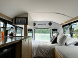 Scenic RV rental bus conversion featuring a comfy bed, kitchenette, and stunning lake and forest views out the rear.