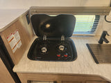 Inside an RV rental: a compact kitchen with a black, two-burner gas stove and sink, ideal for camping adventures.