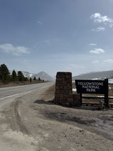 Yellowstone National Park entrance sign and road, with snowy mountains in the distance. Ideal for your next rv rental adventure.