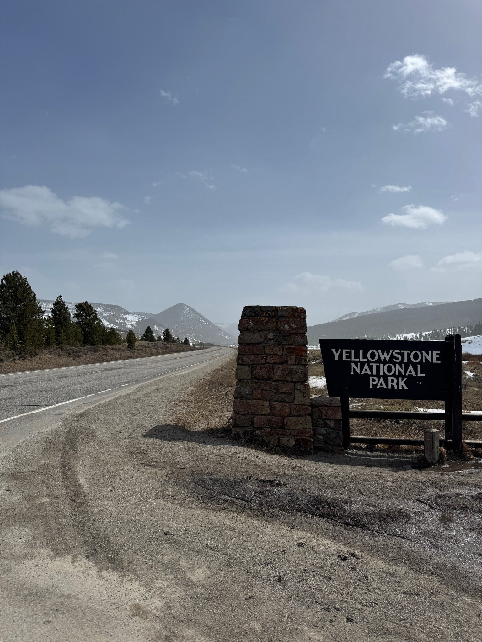 Yellowstone National Park entrance sign and road, with snowy mountains in the distance. Ideal for your next rv rental adventure.