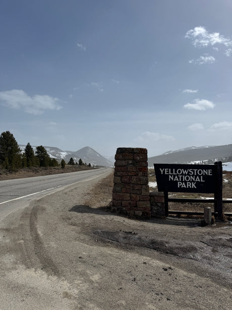 Yellowstone National Park entrance sign and road, with snowy mountains in the distance. Ideal for your next rv rental adventure.