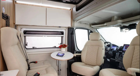Spacious and bright RV rental interior with cream seating, a small dining table, storage, and the driver's cockpit.
