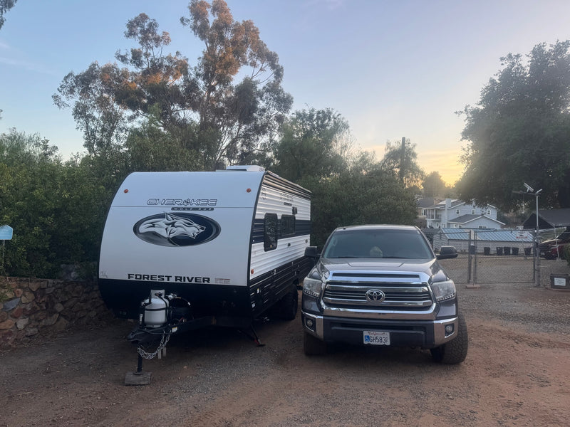 A shiny white Cherokee Wolf Pup RV rental is parked next to a grey Toyota Tundra truck on a dirt lot — photo 1