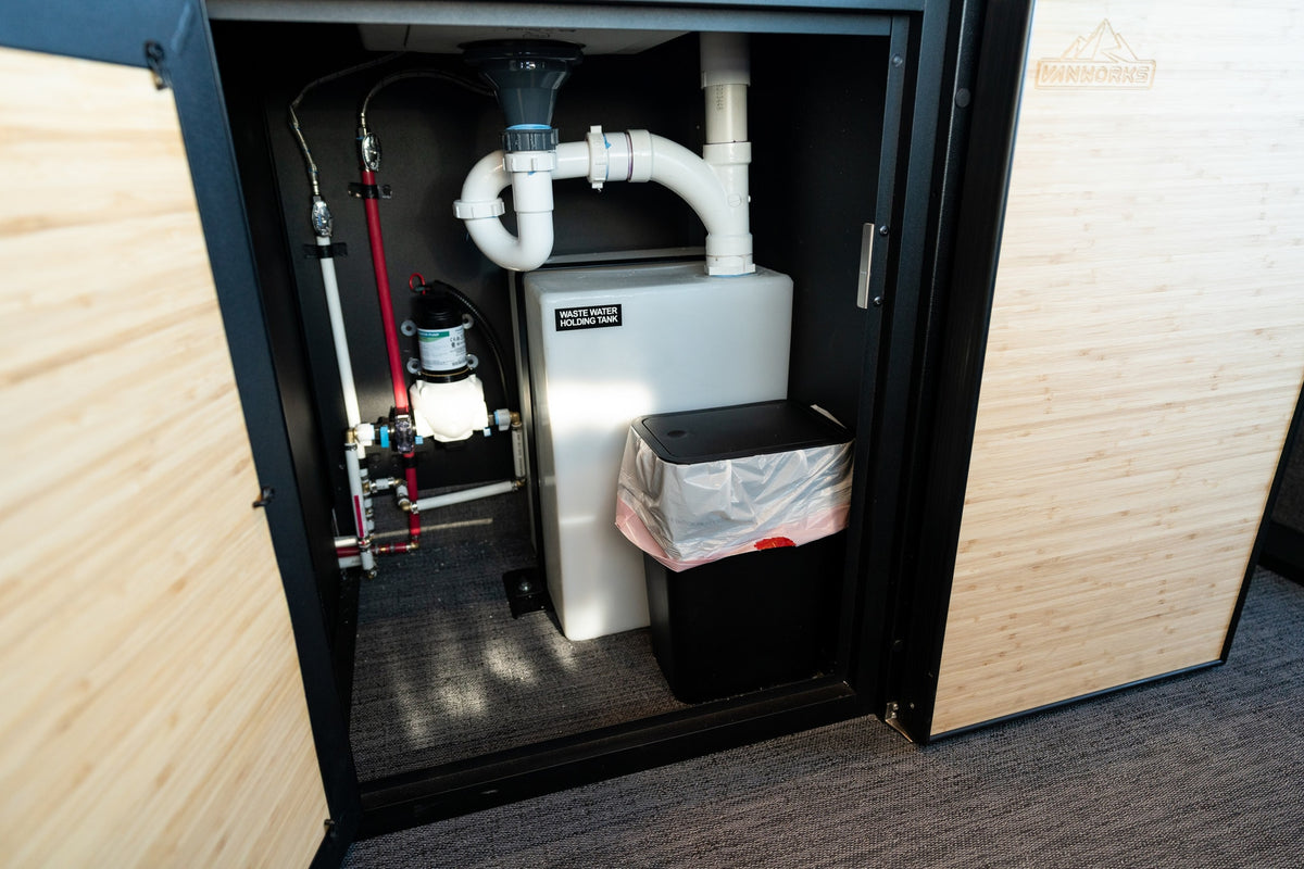 RV rental's compact plumbing, water pump, and waste holding tank with a small bin, efficiently organized within a cabinet. — photo 19