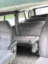 RV rental interior with multiple rows of gray cloth seats, seatbelts, and an overhead LED light strip.