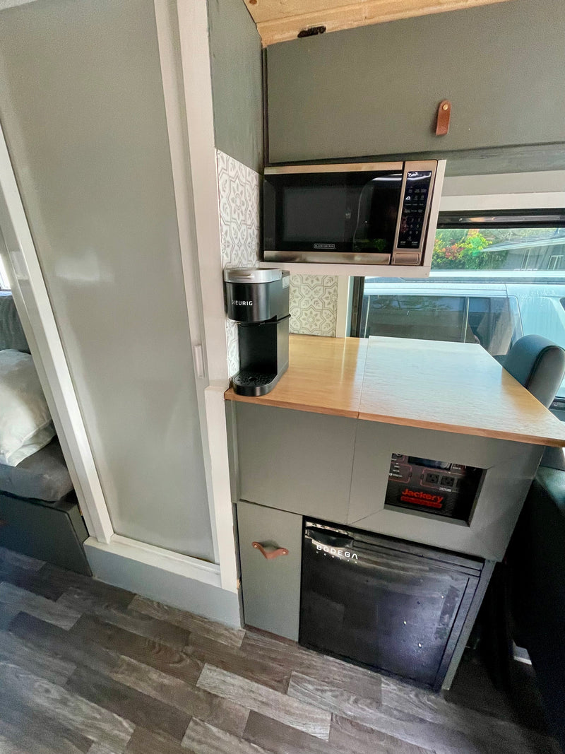 This rv rental features a compact kitchen: microwave, Keurig, Jackery power, Bodega cooler, and dining area. — photo 16