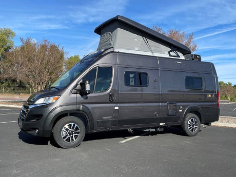 Dark gray Winnebago Solis pop-top camper van for RV rental, parked on asphalt under a clear blue sky.