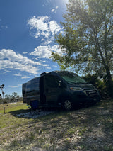 Discover freedom with an rv rental! A dark camper van parked at a sunny campsite under a blue sky.