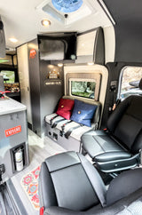 Cozy RV rental interior featuring swivel seats, a bench, kitchen counter, and TV. Ideal for adventurous road trips.