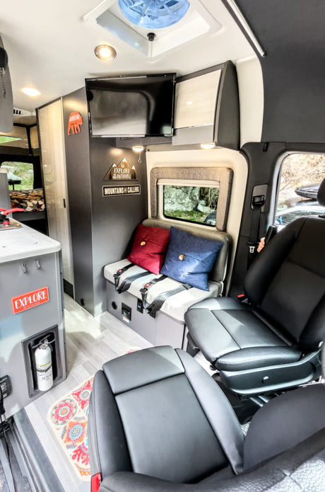 Cozy RV rental interior featuring swivel seats, a bench, kitchen counter, and TV. Ideal for adventurous road trips.