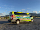 Adventure-ready RV rental van: vibrant custom paint, neon green with a blue/orange mural, parked outdoors with mountains as a backdrop.