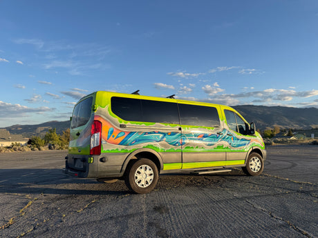 Adventure-ready RV rental van: vibrant custom paint, neon green with a blue/orange mural, parked outdoors with mountains as a backdrop.