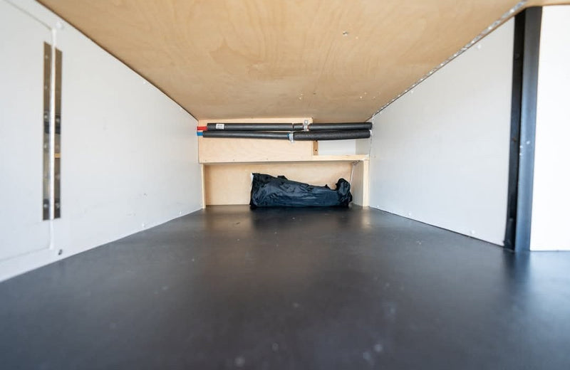 Inside an RV rental: organized under-bed storage with insulated pipes, a small shelf, and a black bag for travel gear. — photo 19